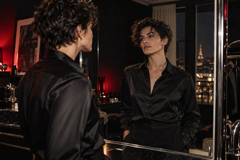 Une personne adulte en tenue noire observe son reflet dans une ambiance nocturne aux accents carmin.