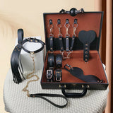 Mallette BDSM Pigalle : mallette ouverte avec accessoires rangés, martinet et laisse à côté, noir
